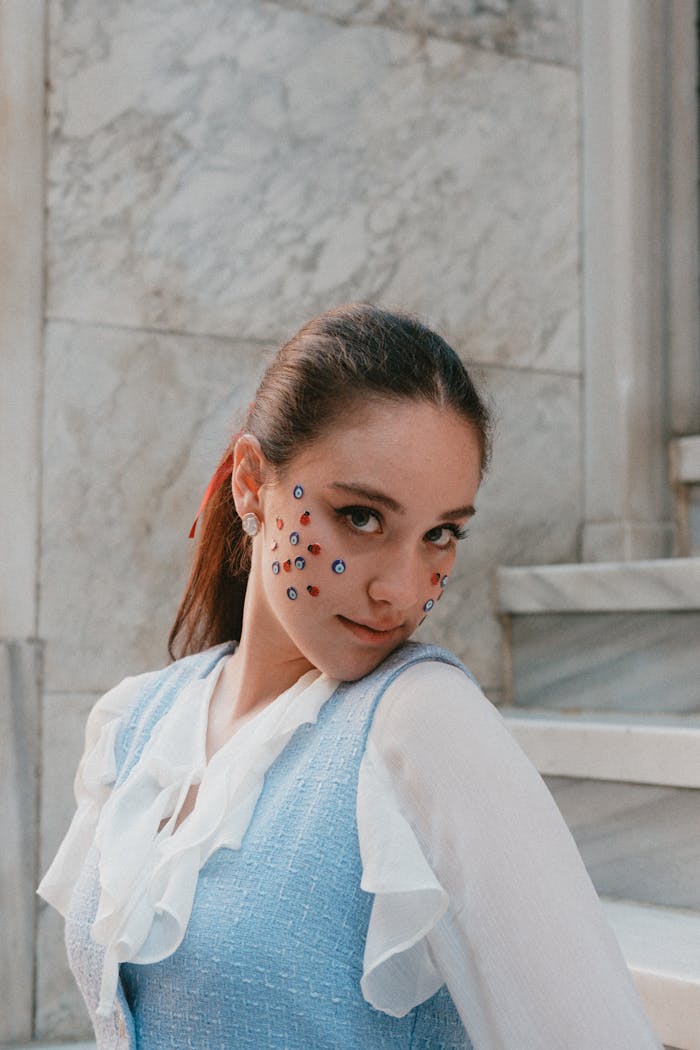 Portrait of a young woman with colorful face decorations, wearing a blue and white outfit.