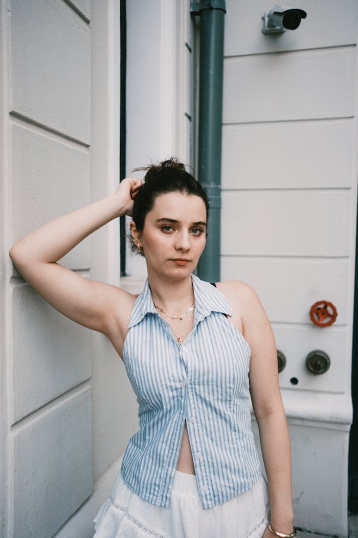 Woman in blue striped top posing confidently by a city wall.